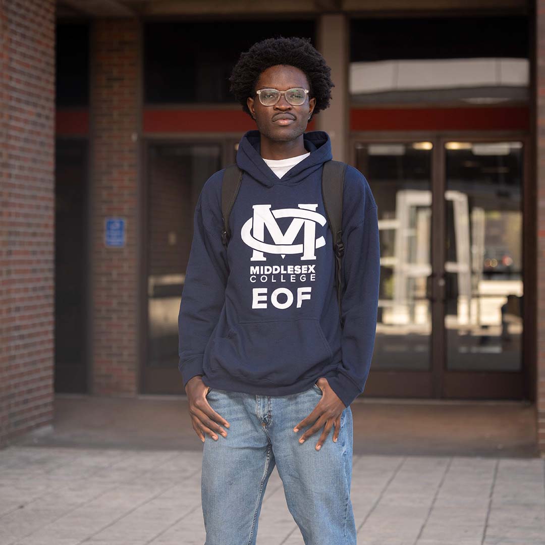 Bill stands for a photograph, wearing an (MC) Middlesex College EOF hoodie.