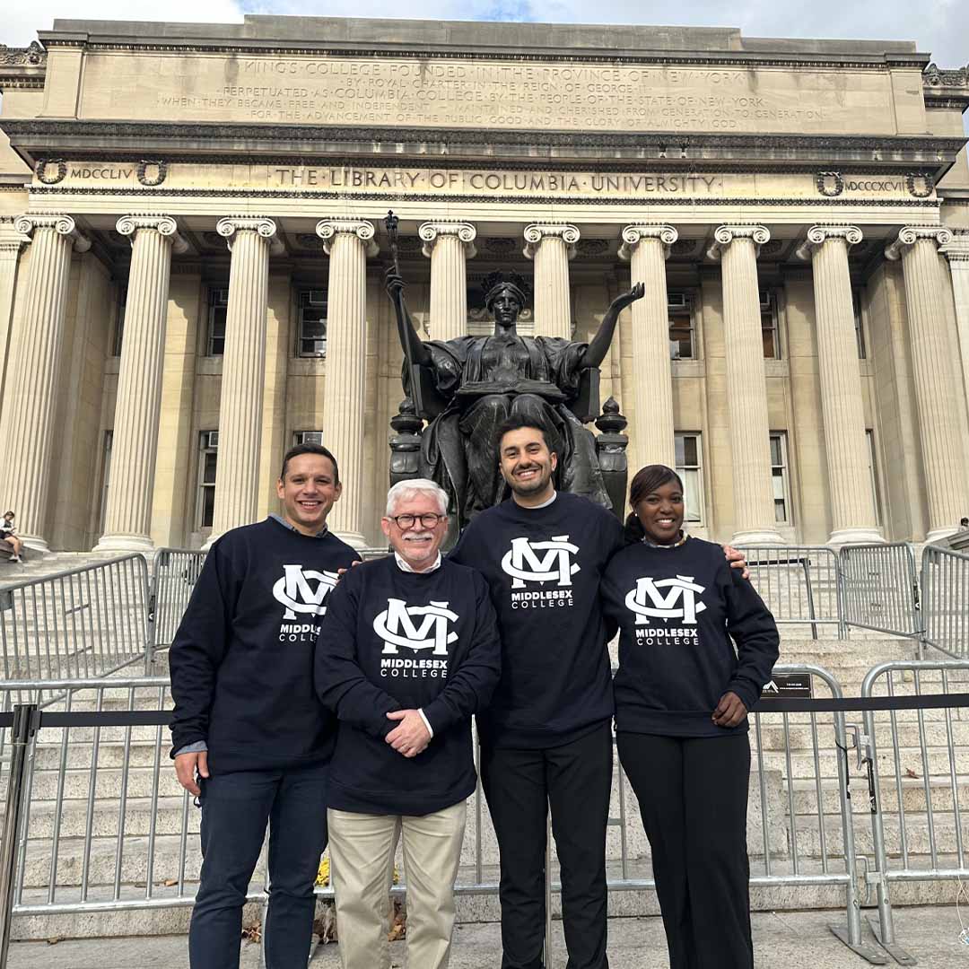 (l-r) Kyle Morgan, Middlesex College President Mark McCormick, Nima Sedghi, and Yokasti Mateo in front of the library of Columbia University. Each person is wearing a Middlesex College sweatshirt.