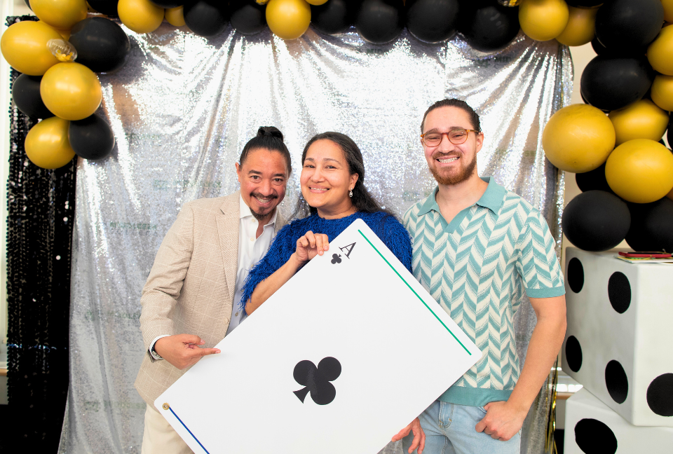 Attendees of the Casino Night holding an oversized ace card surrounded by a balloon arch and themed decor