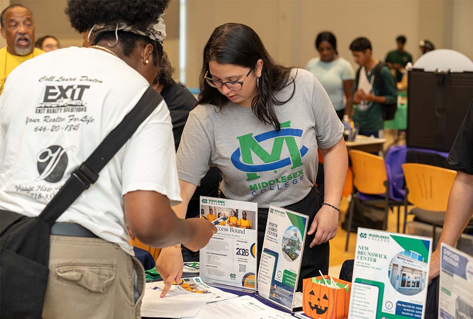 A student in a gray Middlesex College t-shirt stands over a table with informational signs and brochures.