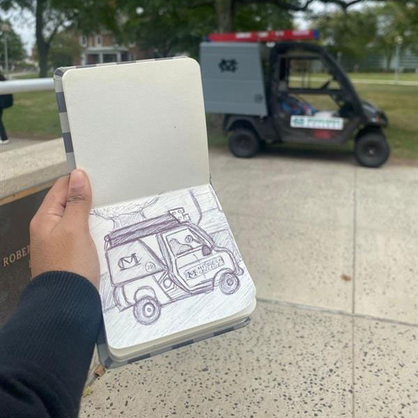 A sketch of a Middlesex College maintenance vehicle held up next to the actual vehicle.