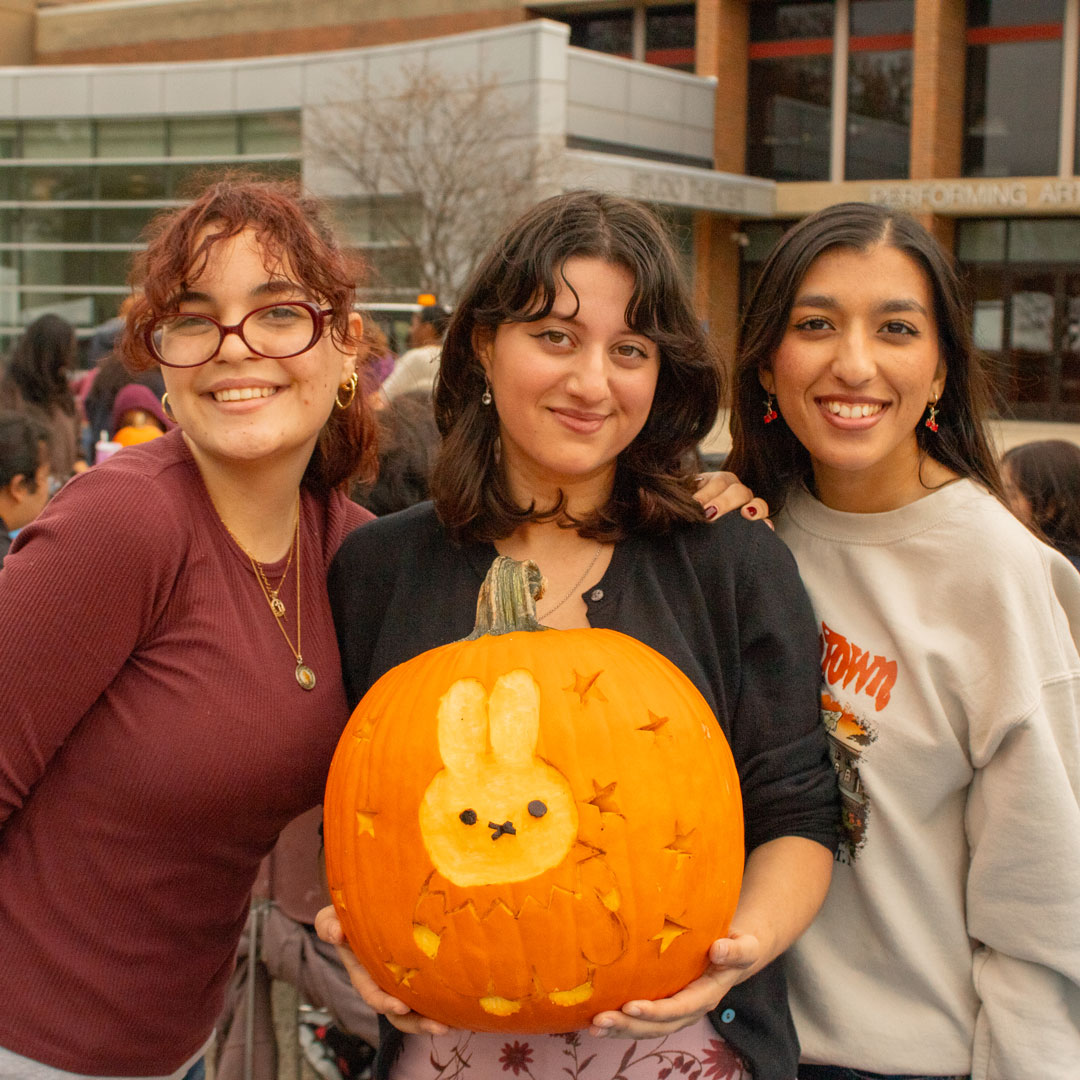 A group of students are holding a carved pumpkin of a bunny.