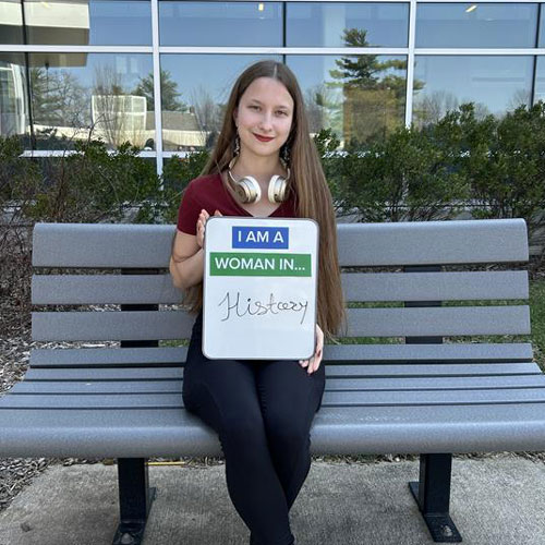 A student holding a sign 'I am a woman in History'.