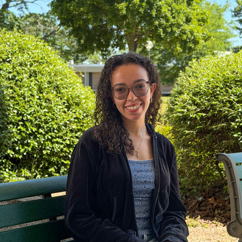 Marah Maisonave, Year of Aesthetics Sidewalk Decal Participant, sitting on a bench in the Quad.