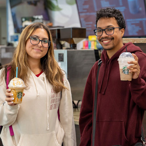 Two students holding Starbucks drinks outside the cafe.